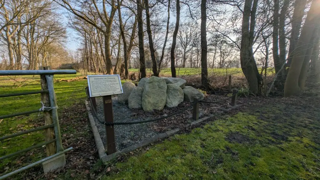 Historische Feldsteine am Totenweg in Padingbüttel, umgeben von Bäumen und einer Informationstafel.