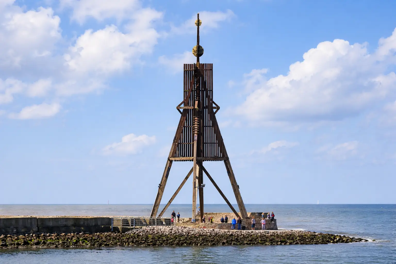 Kugelbake Cuxhaven – hölzernes Seezeichen an der Elbmündung mit Besuchern auf dem Wellenbrecher unter blauem Himmel